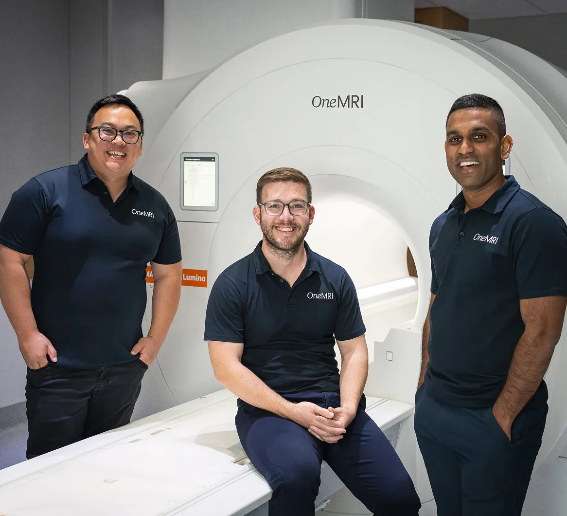 MRI team posing inside scan room with machine